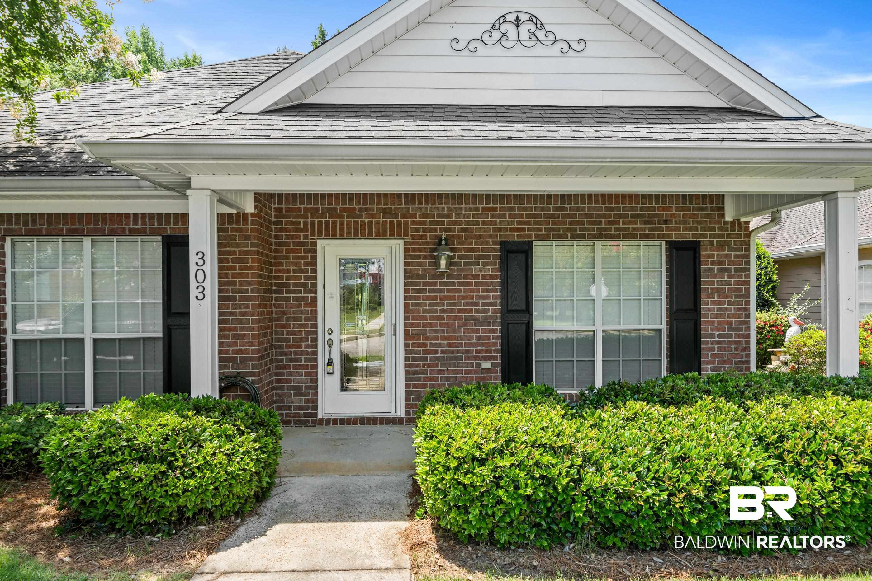 303 Savannah Circle Foley, AL 36535 - Photo 31 of 34 Brick facade residence featuring a covered front porch, white-paneled front door with glass insert, black window shutters, and a decorative gable vent