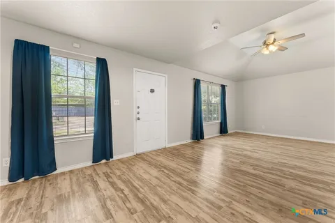 a view of an empty room with wooden floor and a window