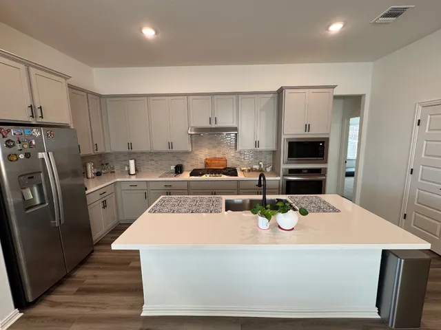 a kitchen with a refrigerator a stove a sink and white cabinets with wooden floor