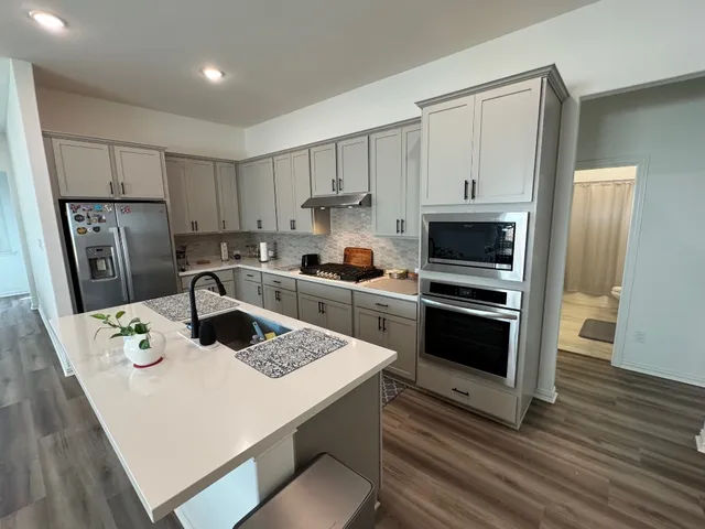 a kitchen with a refrigerator a stove a sink and white cabinets with wooden floor