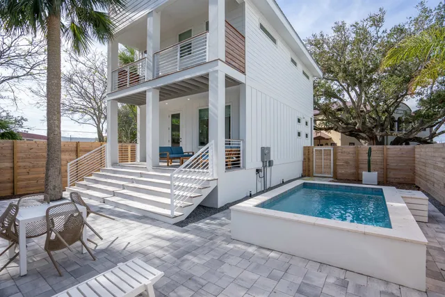 a view of a white house with a large pool and wooden floor and fence