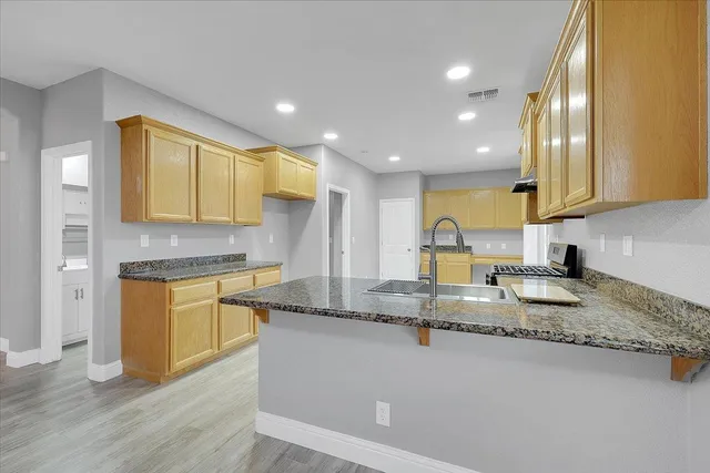 a kitchen with granite countertop a sink a stove cabinets and wooden floor
