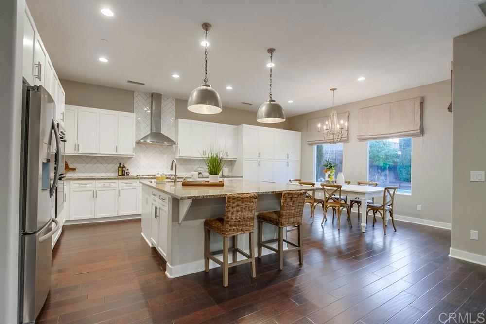 7177 Sitio Corazon Carlsbad, CA 92009 - Photo 14 of 41 a kitchen with a table chairs wooden floors and a view of living room