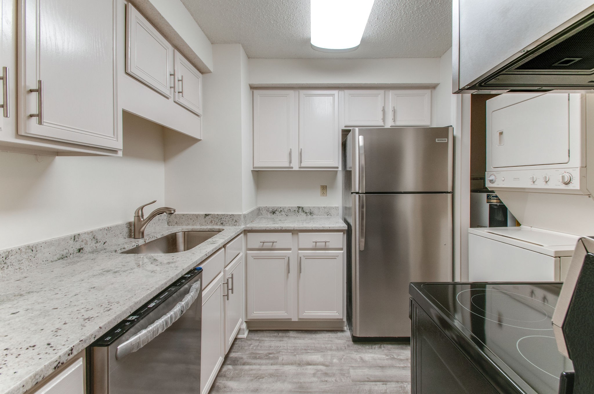 a kitchen with stainless steel appliances granite countertop a refrigerator a stove a sink and white cabinets
