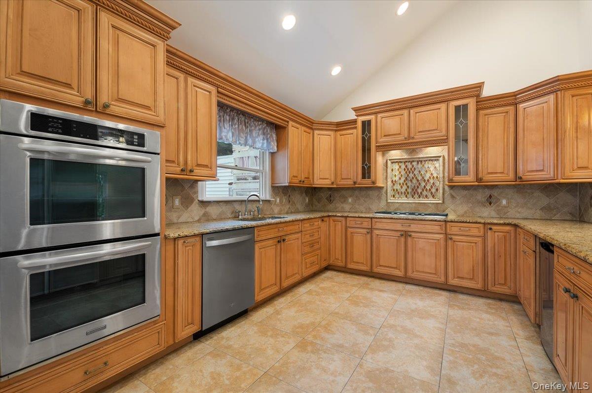 33 Fleets Cove Road Huntington, NY 11743 - Photo 8 of 42 Kitchen with appliances with stainless steel finishes, backsplash, brown cabinetry, high vaulted ceiling, and recessed lighting