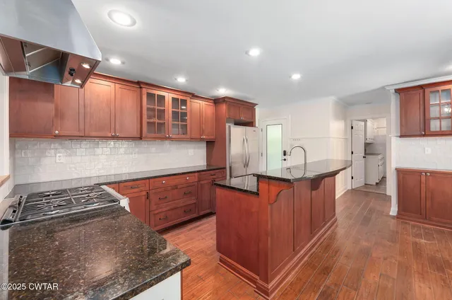 a large kitchen with stainless steel appliances granite countertop a stove a sink dishwasher and a refrigerator with wooden floor