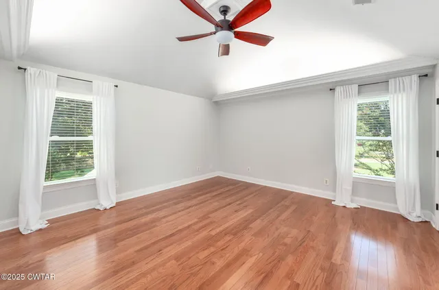 an empty room with wooden floor fan and windows