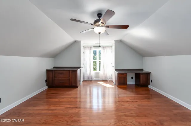 an empty room with wooden floor chandelier fan and windows