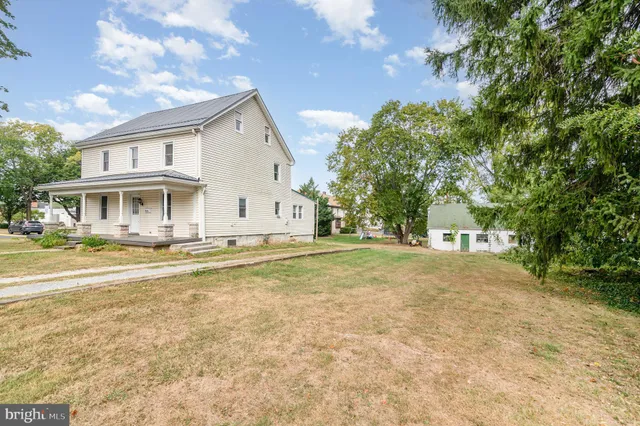 a view of a white house with a large trees with plants and large trees