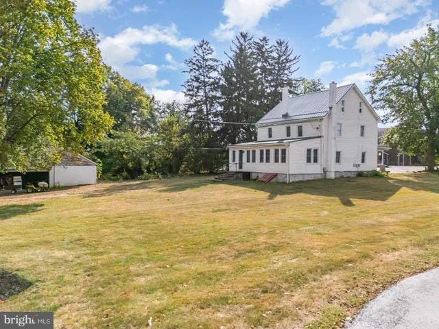 a view of a white house next to a yard with big trees