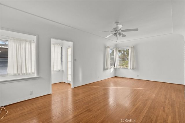 an empty room with wooden floor chandelier fan and windows