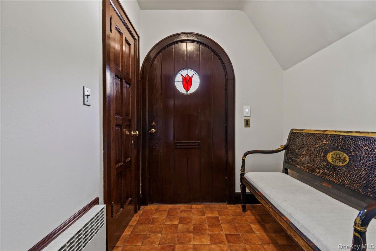 46 Fenimore Road Scarsdale, NY 10583 - Photo 8 of 35 Entrance Foyer has tile flooring, coat closet and plenty of space for removing shoes and boots. Notice the delightful red tulip stained glass window and the arched front door.