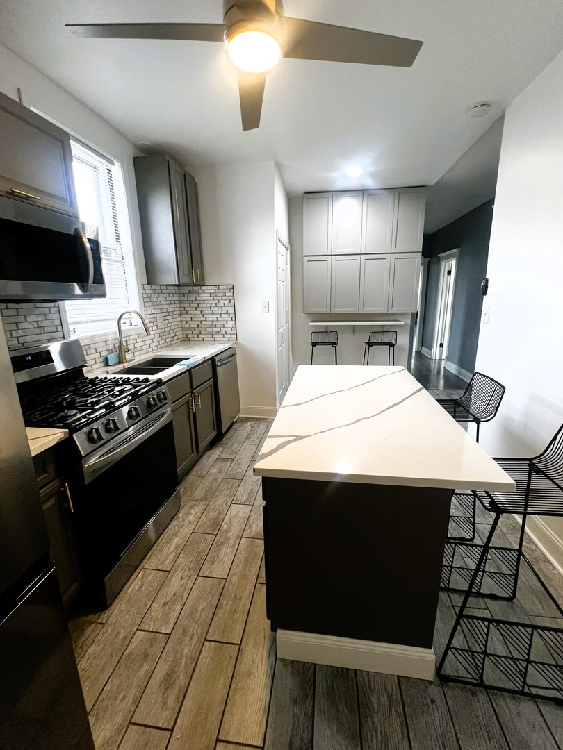 5461 West Haddon Avenue, Unit 2 Chicago, IL 60651 - Photo 7 of 21 a kitchen with stainless steel appliances kitchen island granite countertop a stove a sink and a microwave