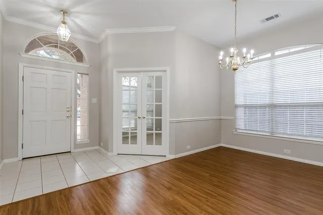 an empty room with wooden floor chandelier and windows
