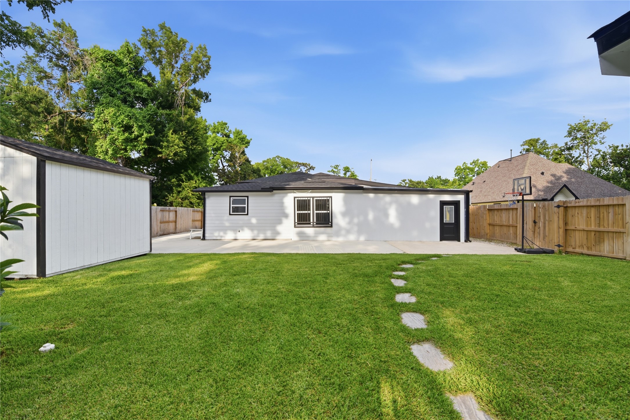 9403 Spaulding Street Houston, TX 77016 - Photo 46 of 50 Spacious backyard featuring a well-maintained lawn, concrete patio area, and storage shed. The yard is fenced for privacy and includes a basketball hoop, ideal for outdoor activities.