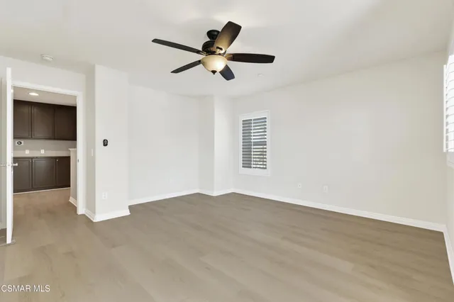 a view of an empty room with wooden floor and a ceiling fan