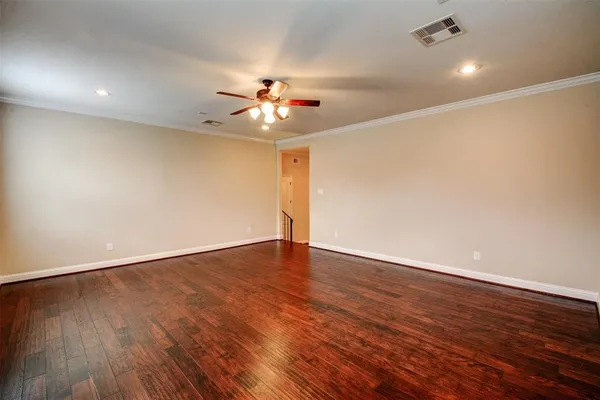 a view of an empty room with wooden floor and a ceiling fan