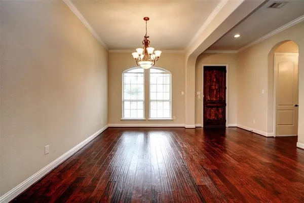 an empty room with wooden floor chandelier and windows