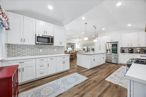 a large kitchen with stainless steel appliances granite countertop a stove a sink dishwasher a microwave oven with cabinets and wooden floor