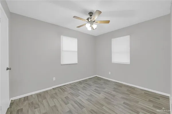 a view of an empty room with wooden floor and a ceiling fan