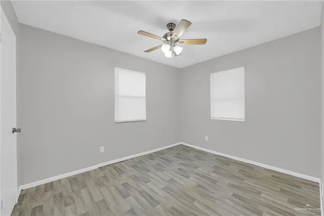 a view of an empty room with wooden floor and a ceiling fan