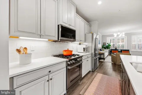 a kitchen with stainless steel appliances granite countertop a sink dishwasher stove and white cabinets with wooden floor