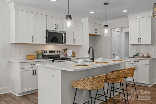 a kitchen with stainless steel appliances granite countertop a sink a stove a refrigerator and white cabinets with wooden floor