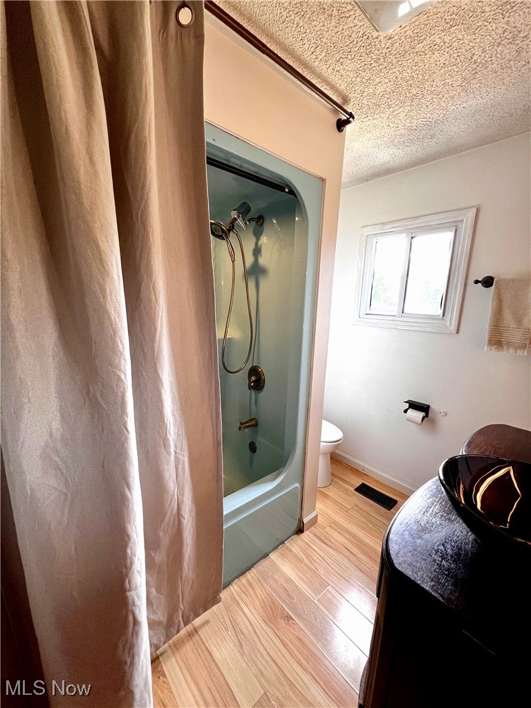 54340 Bracken Road Bridgeport, OH 43912 - Photo 16 of 29 Bathroom featuring shower / bathtub combination with curtain, toilet, wood-type flooring, and a textured ceiling