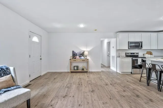 a kitchen with stainless steel appliances granite countertop a stove a refrigerator a microwave a sink and white cabinets with wooden floor