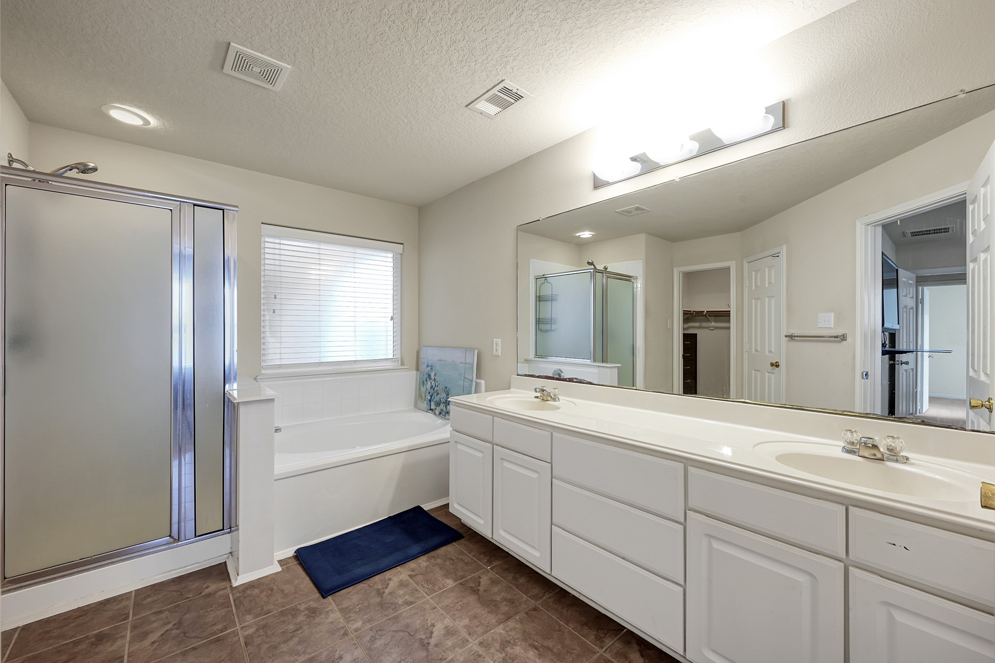 22518 Goss Spring Court Spring, TX 77373 - Photo 11 of 19 This spacious bathroom features a large mirror above dual sinks, a separate glass-enclosed shower, and a bathtub with natural light from the window. The neutral color palette and tile flooring offer a clean, contemporary feel.