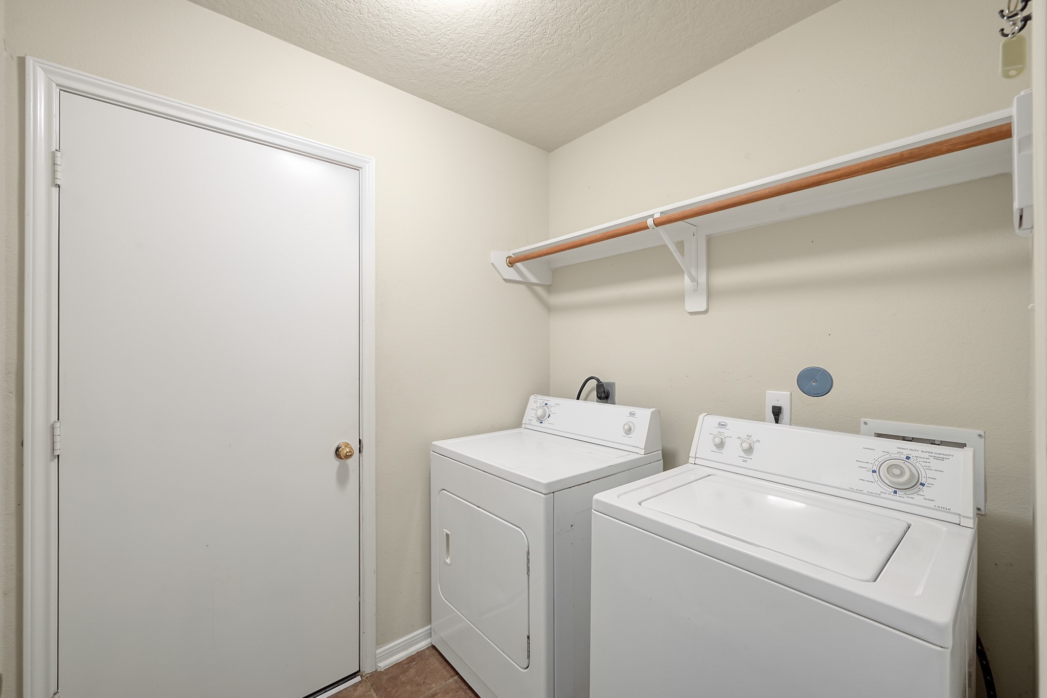 22518 Goss Spring Court Spring, TX 77373 - Photo 15 of 19 This photo shows a compact laundry room with a washer and dryer side by side. There's a shelf above for storage, and the walls are painted a light neutral color. The room is well-lit and has a simple, functional design.