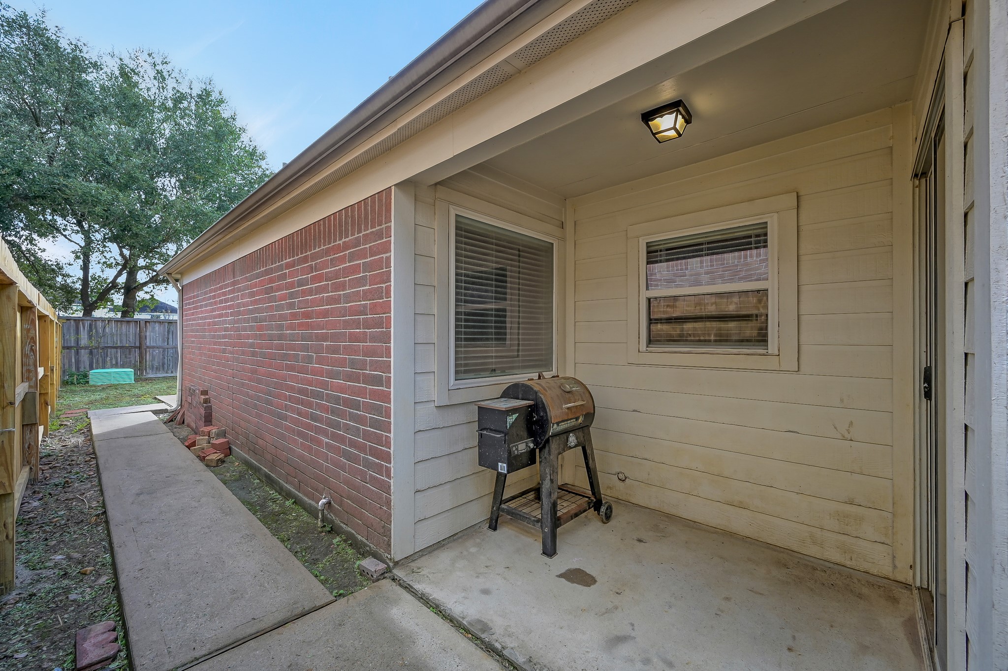22518 Goss Spring Court Spring, TX 77373 - Photo 17 of 19 This photo shows a cozy backyard area with a covered patio, featuring a small barbecue grill. It has a mix of brick and siding exterior, and a concrete walkway leading to a fenced yard with trees in the background.