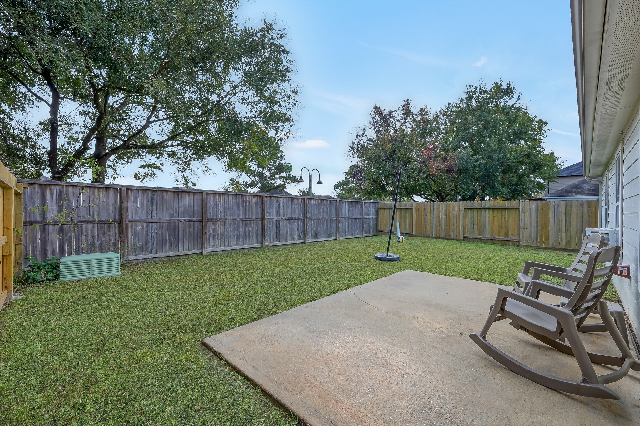 22518 Goss Spring Court Spring, TX 77373 - Photo 18 of 19 Spacious backyard featuring a well-maintained lawn, a concrete patio with rocking chairs, and a tall wooden fence for privacy. Ideal for relaxation and outdoor activities.