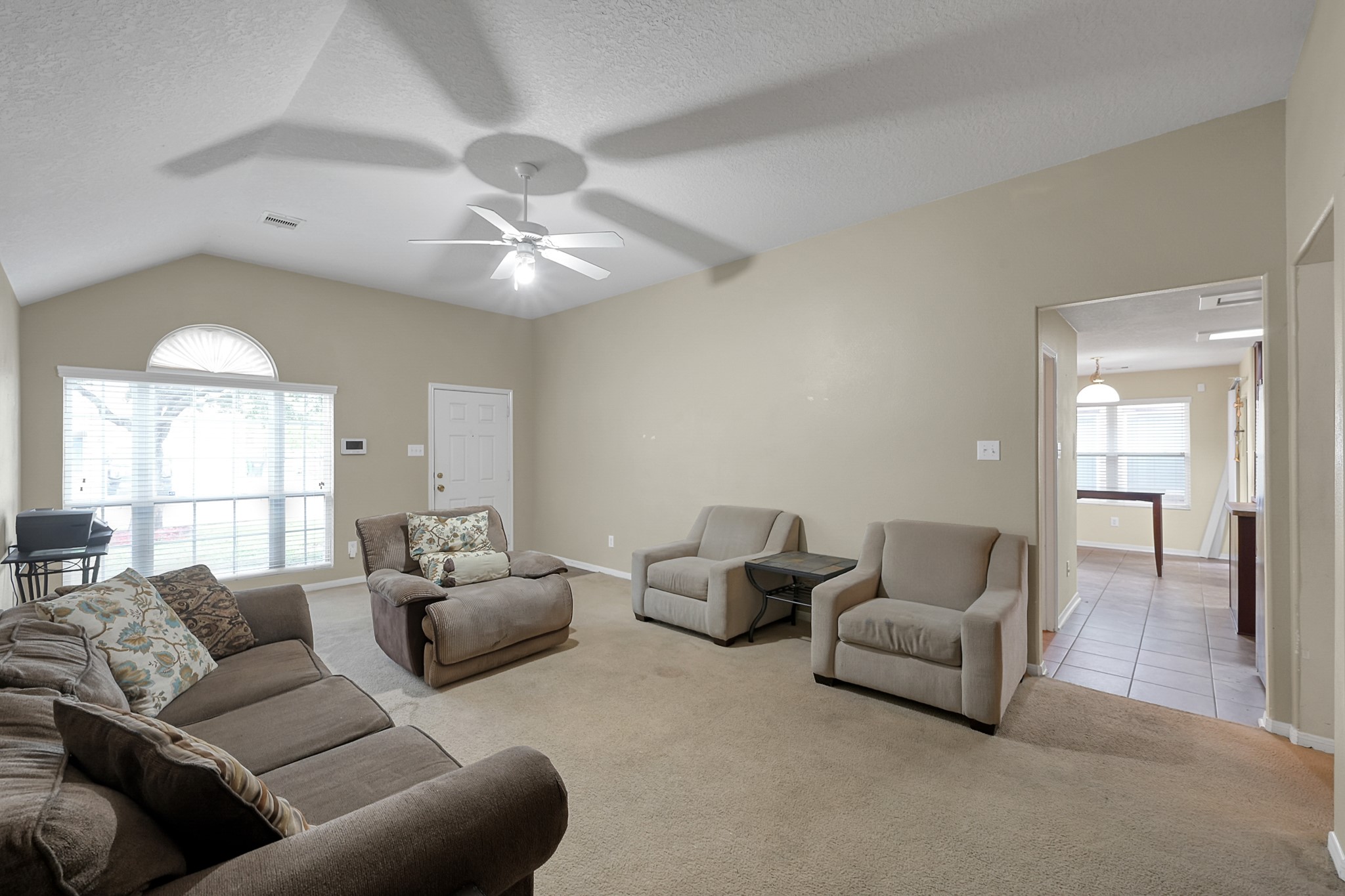 22518 Goss Spring Court Spring, TX 77373 - Photo 4 of 19 This living room features neutral walls and carpet, a ceiling fan, and ample seating with a large window providing natural light. It opens to a tiled dining area, creating a spacious and inviting atmosphere.