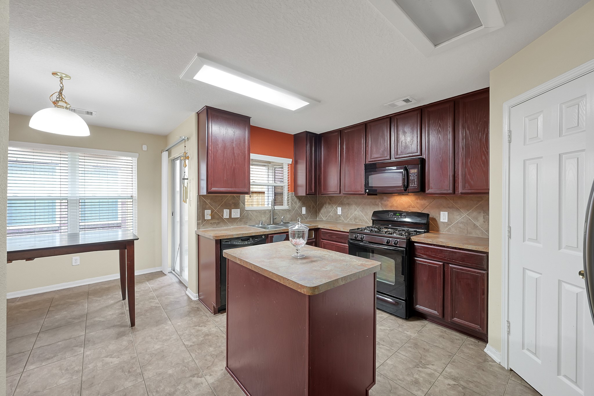 22518 Goss Spring Court Spring, TX 77373 - Photo 5 of 19 This kitchen features rich wood cabinets, a central island, and modern appliances. It has tiled flooring and ample natural light from large windows and a glass door leading outside. The space also includes a dining area with a hanging light fixture.