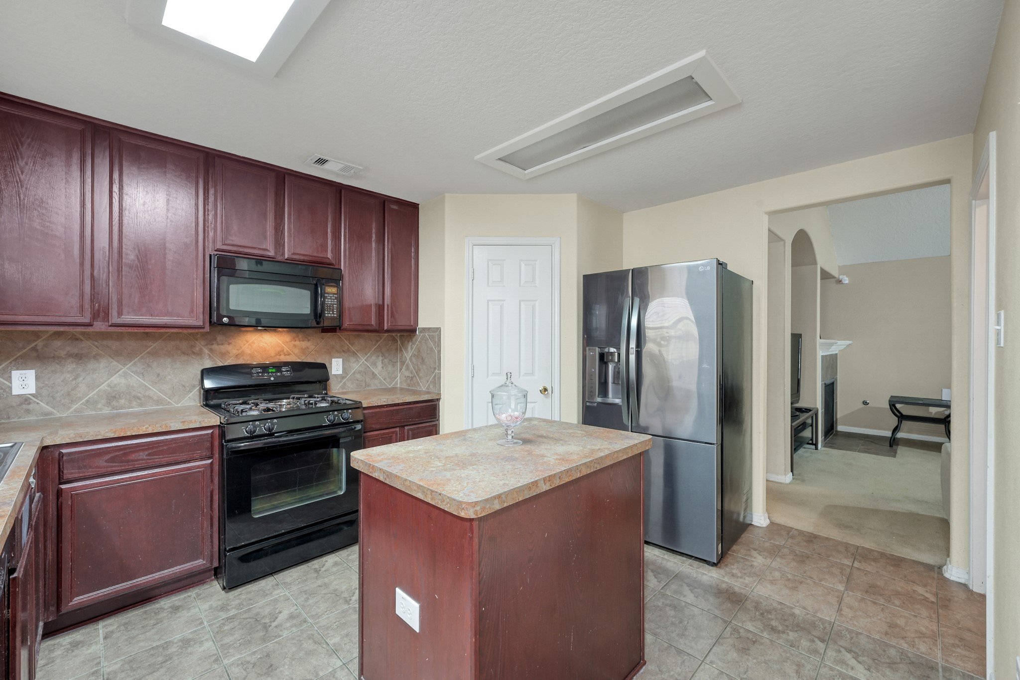 22518 Goss Spring Court Spring, TX 77373 - Photo 6 of 19 This kitchen features dark wood cabinetry, stainless steel refrigerator and a black gas stove with a microwave above. The space has tiled flooring and opens into the living area, creating a seamless flow.