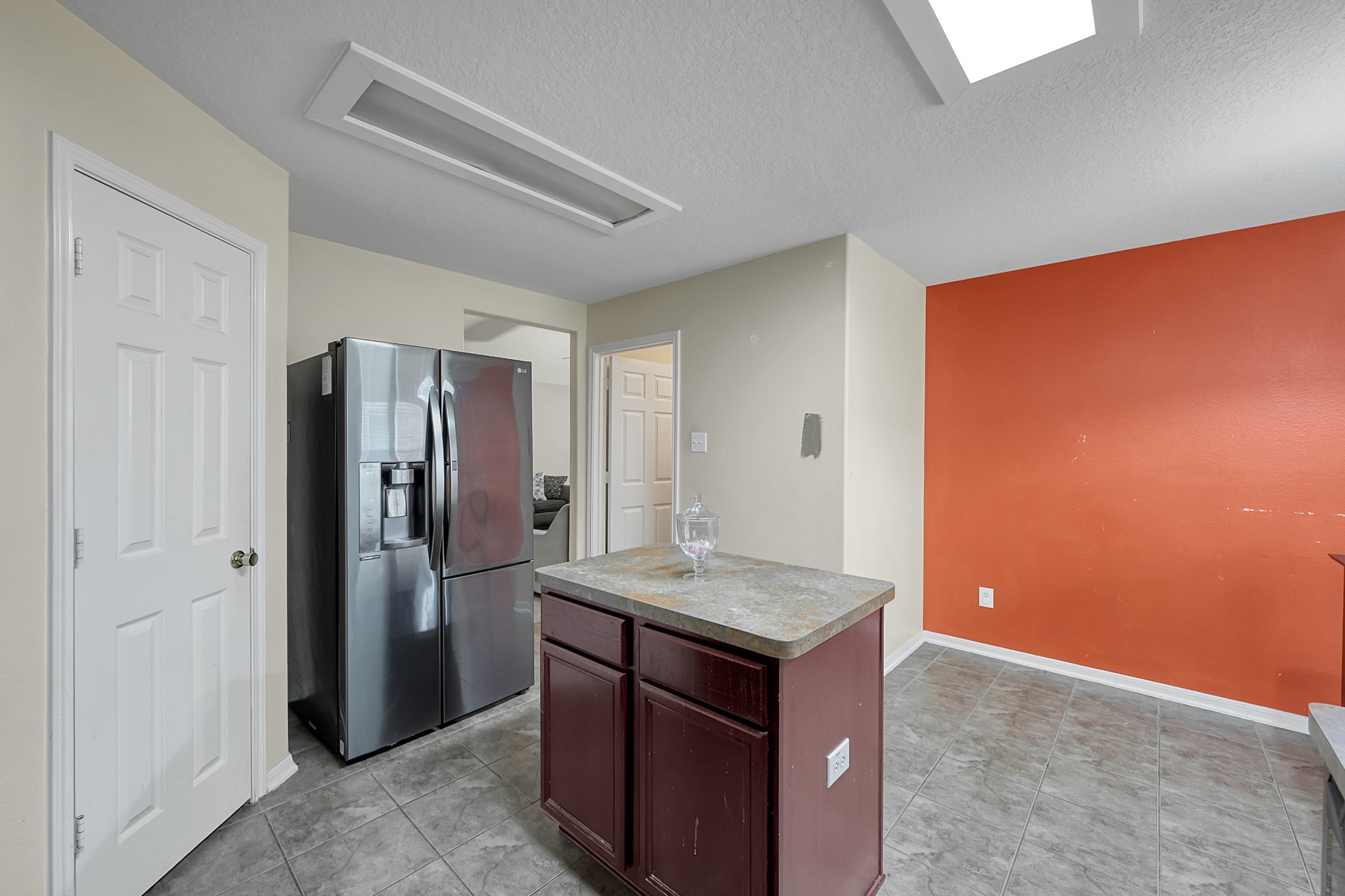 22518 Goss Spring Court Spring, TX 77373 - Photo 7 of 19 This kitchen features a modern stainless steel refrigerator, a central island with a countertop, and a vibrant orange accent wall. The room is well-lit with overhead lighting and has tiled flooring, offering a spacious and functional layout.