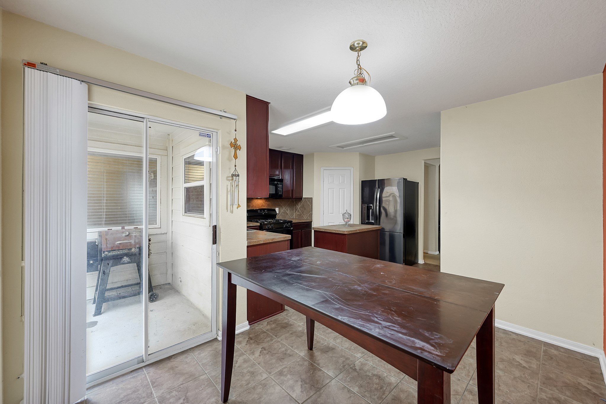 22518 Goss Spring Court Spring, TX 77373 - Photo 9 of 19 This photo showcases a bright kitchen area with tile flooring and neutral walls. It features a dark wood dining table, modern hanging light fixture, and sliding glass doors leading to a covered patio. The kitchen includes dark cabinetry, a sleek refrigerator, and a gas stove.