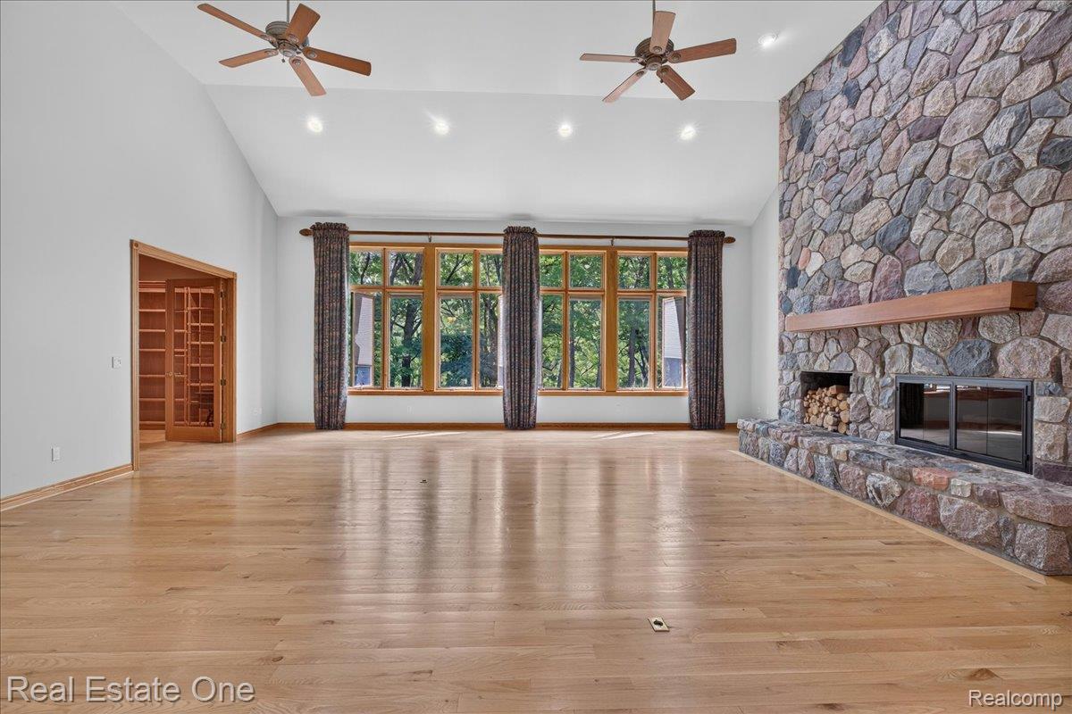 425 Courtney Road Leonard, MI 48367 - Photo 10 of 89 Spacious room featuring vaulted ceilings, wood-finish flooring, and a floor-to-ceiling stone fireplace with a wood mantle