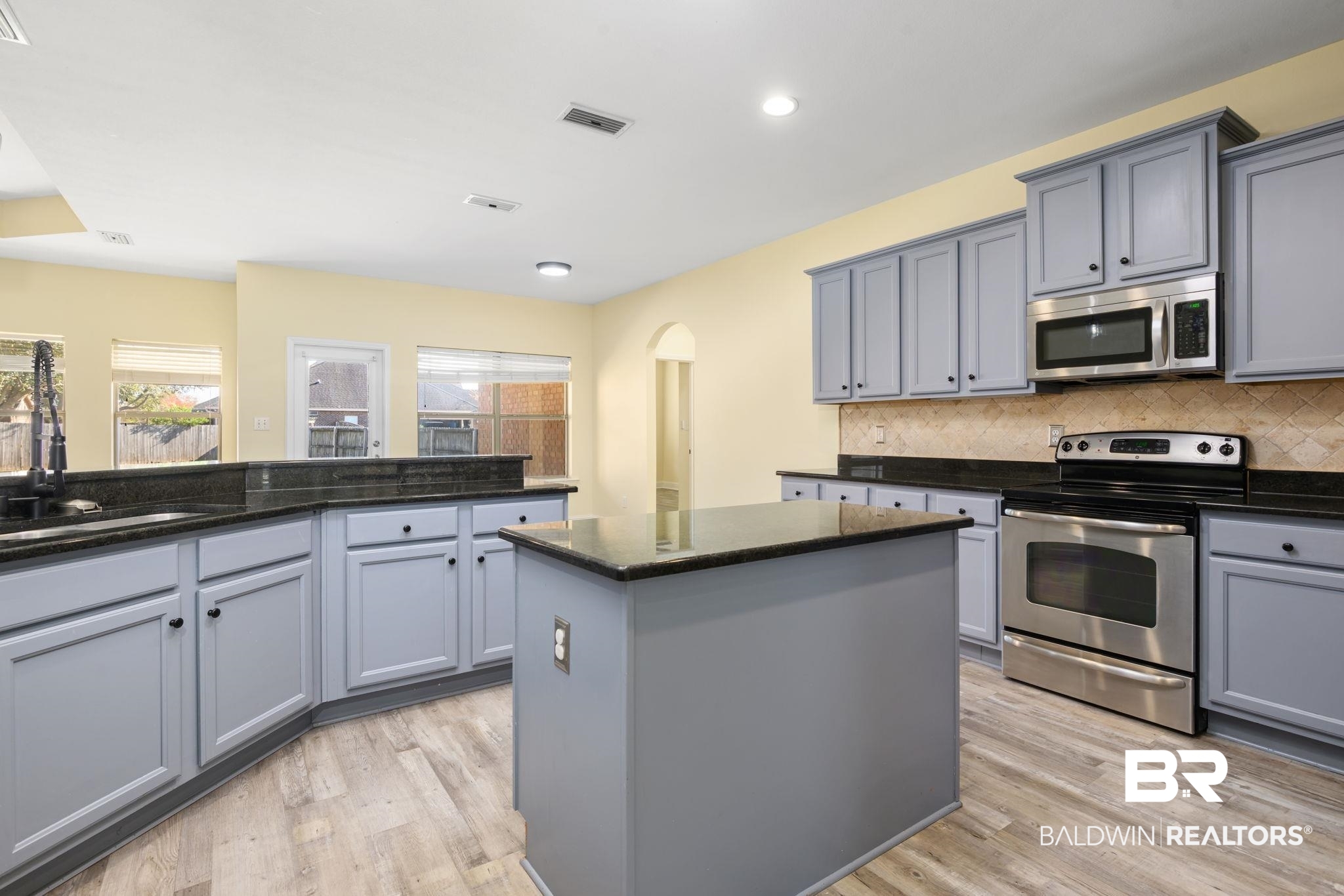 25234 Fairfax Road Daphne, AL 36526 - Photo 16 of 45 Kitchen with gray cabinetry, stainless steel appliances, arched walkways, a kitchen island, and dark stone counters
