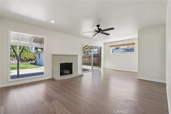 an empty room with wooden floor a ceiling fan a fireplace and windows