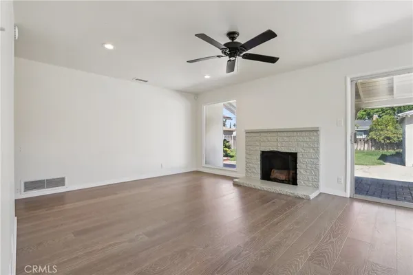 a view of a livingroom with a fireplace a ceiling fan and wooden floor