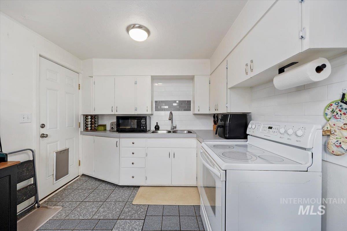 347 Polk Street Twin Falls, ID 83301 - Photo 11 of 25 Kitchen with white electric stove, white cabinetry, light countertops, decorative backsplash, and black microwave