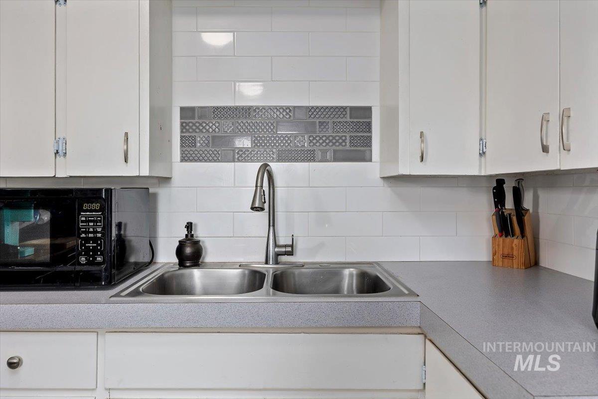 347 Polk Street Twin Falls, ID 83301 - Photo 12 of 25 Kitchen featuring black microwave, white cabinetry, light countertops, and decorative backsplash