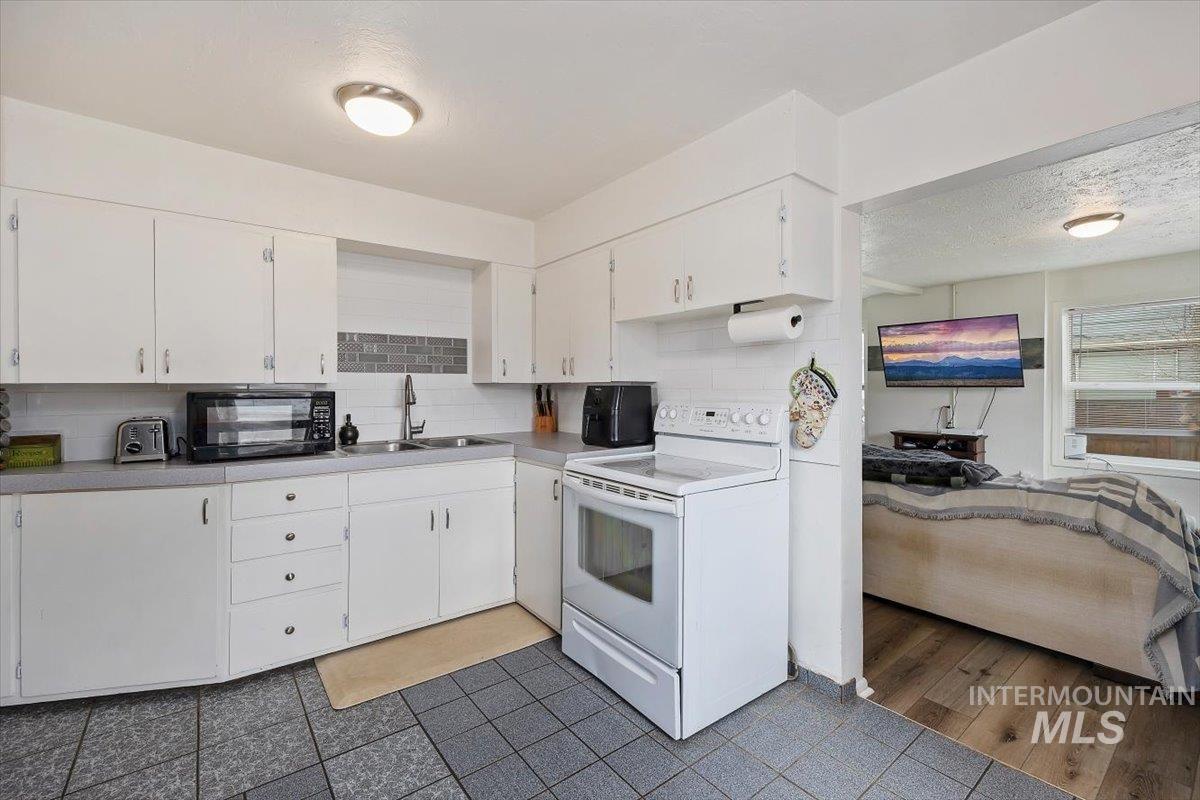 347 Polk Street Twin Falls, ID 83301 - Photo 10 of 25 Kitchen featuring white range with electric cooktop, white cabinetry, decorative backsplash, and a textured ceiling