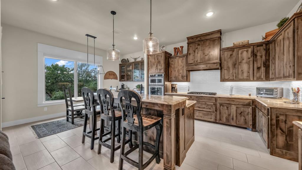 1320 Post Oak Road Gordon, TX 76453 - Photo 17 of 40 Kitchen with decorative backsplash, an island with sink, a breakfast bar area, pendant lighting, and brown cabinets
