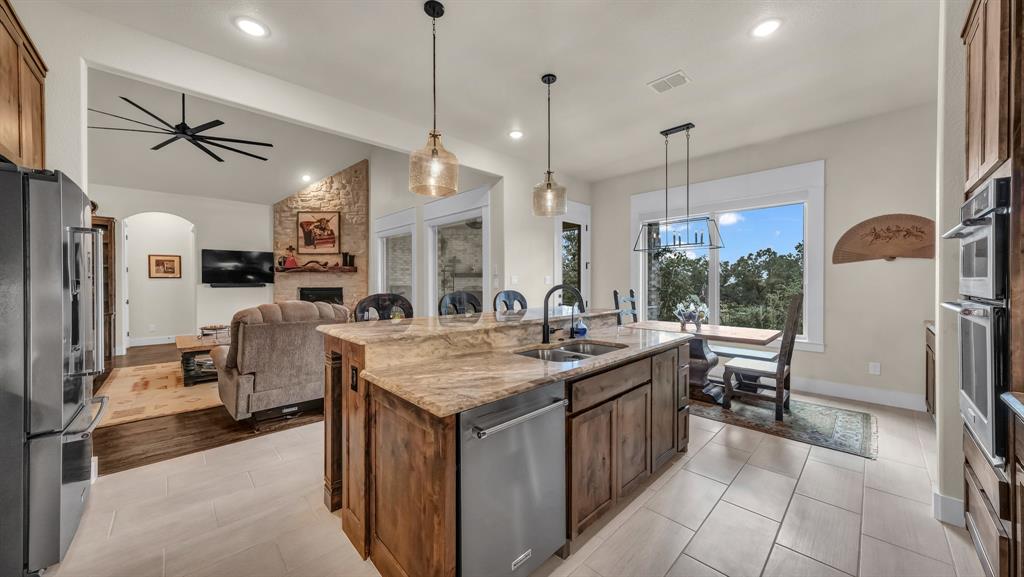 1320 Post Oak Road Gordon, TX 76453 - Photo 19 of 40 Kitchen featuring light stone countertops, appliances with stainless steel finishes, hanging light fixtures, a center island with sink, and vaulted ceiling