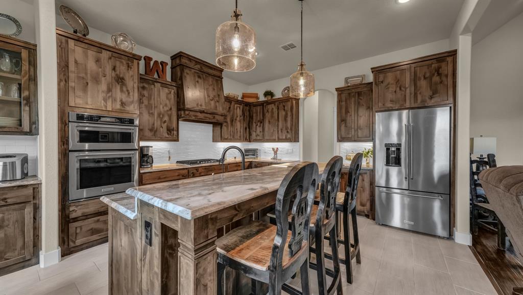 1320 Post Oak Road Gordon, TX 76453 - Photo 21 of 40 Kitchen featuring tasteful backsplash, appliances with stainless steel finishes, decorative light fixtures, an island with sink, and a kitchen bar