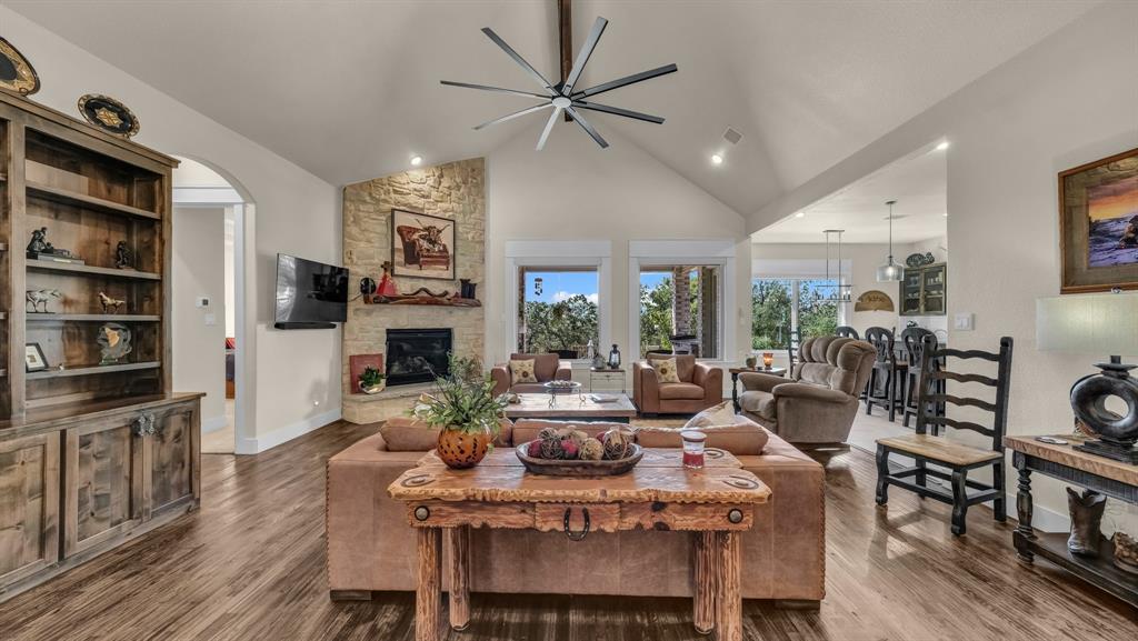 1320 Post Oak Road Gordon, TX 76453 - Photo 10 of 40 Living area with wood finished floors, a stone fireplace, ceiling fan, high vaulted ceiling, and arched walkways