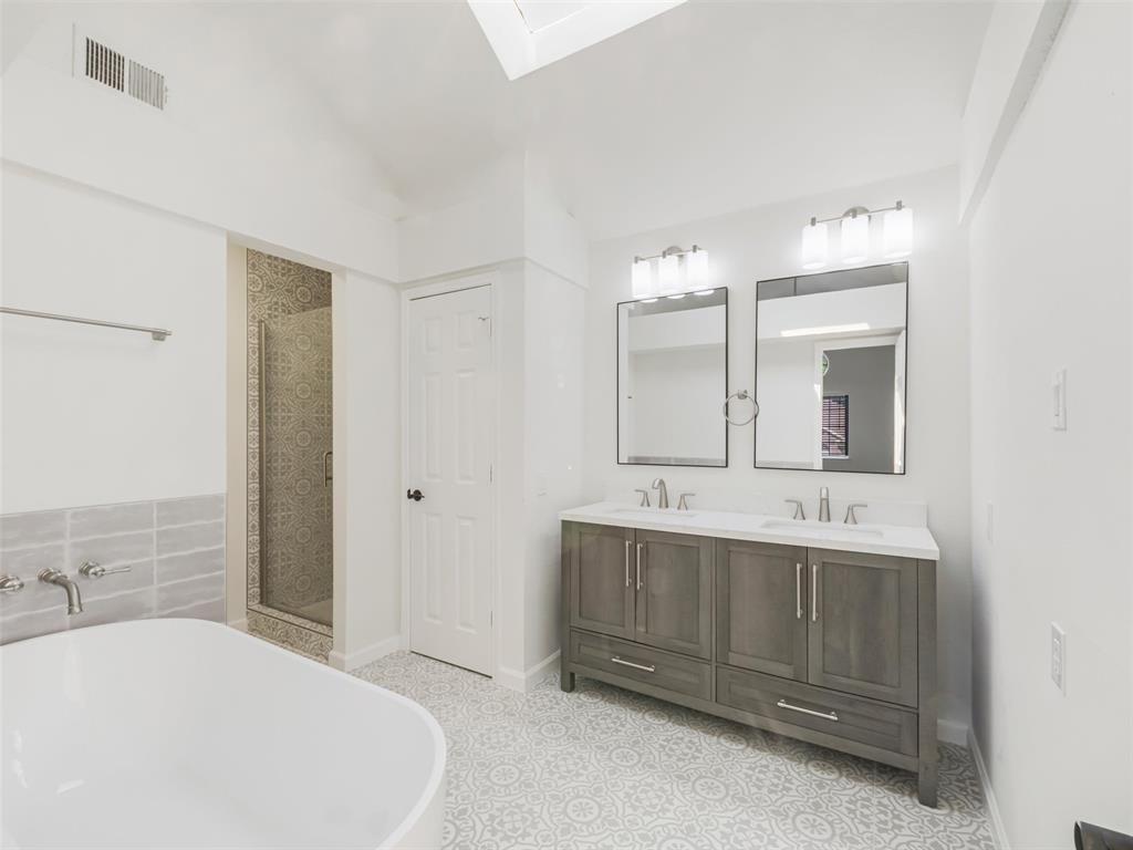 2327 North Ridge Road McKinney, TX 75072 - Photo 19 of 26 Spacious bathroom featuring a double vanity with ample storage, a freestanding soaking tub, a glass-enclosed shower, patterned floor tiling, and a skylight